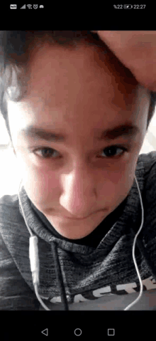 a young boy wearing headphones and a hoodie is taking a selfie with his hand on his forehead .