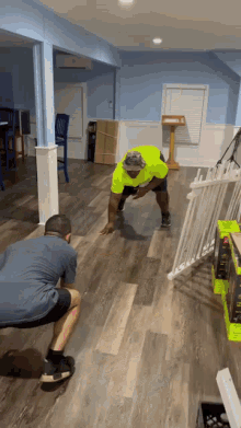 a man in a yellow shirt is squatting on a wooden floor