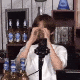 a man is covering his face with his hands while sitting in front of a microphone .