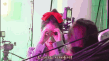 a woman with a red bow in her hair looks through binoculars in front of a camera