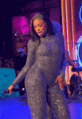 a woman in a silver jumpsuit is singing into a microphone on stage .