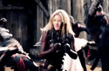 a woman in a white dress is holding a gun in front of a group of men .