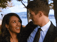 a man and a woman are looking at each other with a lake in the background