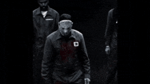 a black and white photo of a man wearing a mask with the letter e on his chest