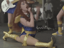 a woman in a superhero costume is kneeling down and singing into a microphone