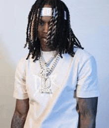a young man with dreadlocks is wearing a white t-shirt and a necklace .