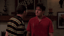 a man in a red shirt is pointing at another man in front of a poster that says ' uebb ' on it