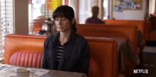 a woman sits at a diner table with a netflix logo on the bottom