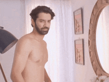 a shirtless man stands in front of a mirror and a lamp