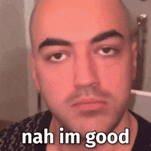 a bald man with a beard is making a funny face with the words `` nah im good '' written on his face .
