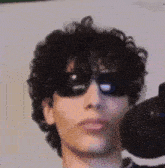 a man with curly hair wearing sunglasses and a microphone .