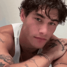 a close up of a man 's face with tattoos on his arms and chest .