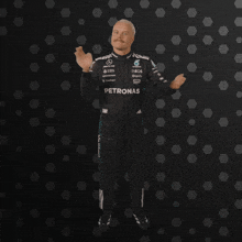 a man in a petronas uniform stands in front of a dark background
