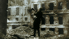 a black and white photo of a man standing in front of a destroyed building with the word krakow on the bottom