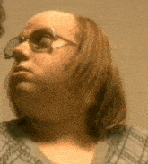 a woman with long hair and glasses is looking at herself in a mirror .