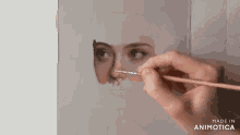 a person is painting a woman 's face with a brush and the words made in animotica are on the bottom