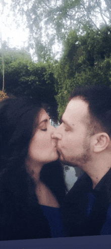 a man and woman are kissing in front of trees