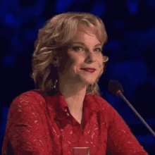 a woman in a red shirt is sitting in front of a microphone and smiling