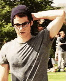 a young man wearing glasses and a beanie holds his hand to his head
