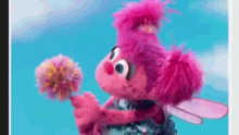 a pink sesame street character is holding a flower in her hands .