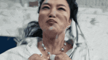 a close up of a woman wearing a pearl necklace making a funny face