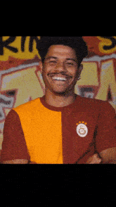 a man wearing a red and yellow shirt with the letter g on it smiles