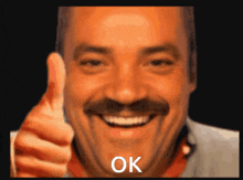 a man with a mustache is smiling and giving a thumbs up with the word ok written below him