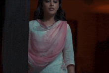 a woman wearing a white top and a pink scarf stands in a dark room