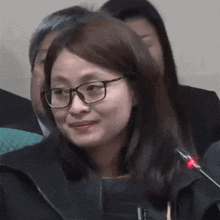 a woman wearing glasses and a black jacket is smiling