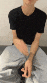 a man in a black t-shirt is sitting down with his hands folded