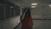 a woman in an orange shirt is walking down a hallway with a lot of windows