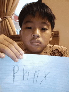 a young boy is holding up a piece of paper with the word phmx written on it