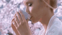 a woman is drinking from a cup with flowers in the background .