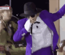 a man in a purple suit and hat is dancing in a room .
