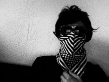 a black and white photo of a person wearing sunglasses and a striped scarf around their face