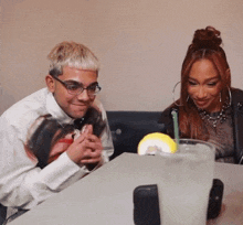 a man and a woman sit at a table looking at a phone