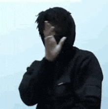 a man in a hooded jacket is covering his face with his hands .