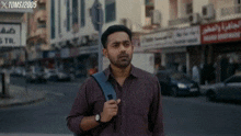 a man with a backpack is walking down a street with a sign that says toms 2005 in the background