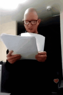 a bald man wearing glasses is reading a paper