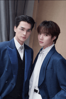 two young men wearing blue suits and white shirts pose for a photo