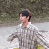 a young man in a plaid shirt is walking down the street with his arms outstretched .