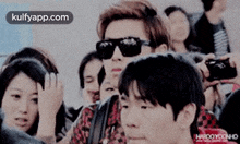 a man wearing sunglasses stands in a crowd of people