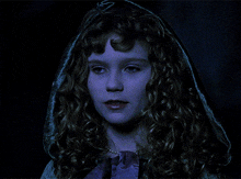 a woman with curly hair and a hood on her head looks at the camera
