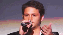 a man in a suit is singing into a microphone while clapping