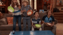 a family is sitting on a couch eating popcorn and watching a game .