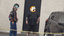 two men are standing in front of a black car with the word $ dood written on it