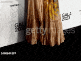 a woman in a long dress is standing in front of a wall with gala 2023 written on it