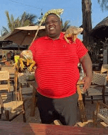 a man in a red striped shirt is holding a lizard on his head .