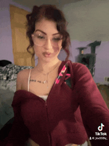a woman with glasses and a tattoo on her chest is wearing a red hoodie