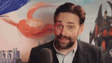 a man with a beard is speaking into a microphone in front of a painting
